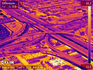 The infrared image shows the hottest and coolest parts of a highway interchange during the day. The yellow/orange areas are hotter and the blue/purple areas are cooler.