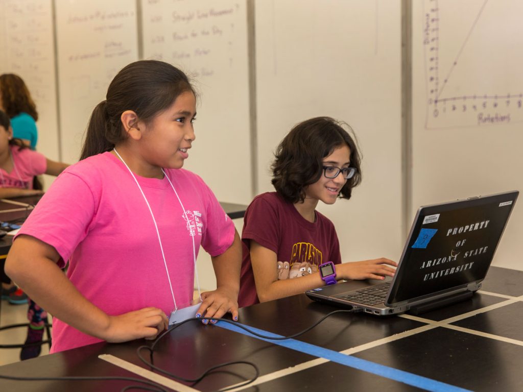 Two girls work at a laptop to program their robot.