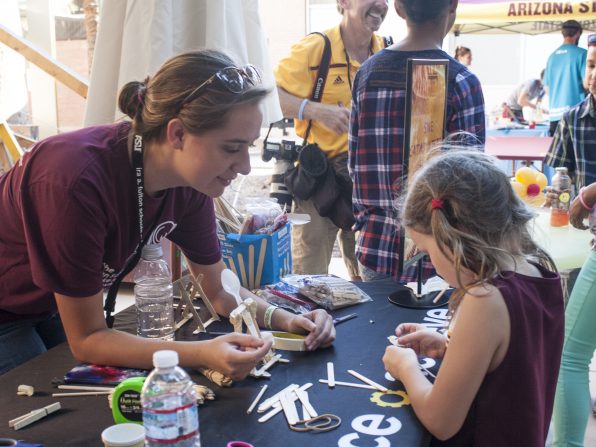 A member of ASU's chapter of the Society of Women Engineers helps a visitor construct a catapult out of household materials at the Fulton Schools' Block Party, Oct. 22, 2016. Photographer: Erik Wirtanen/ASU