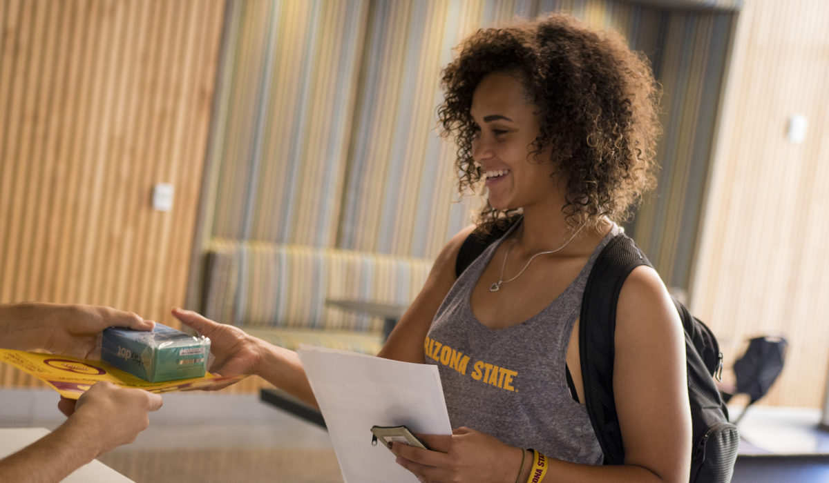Photo of a girl being handed a box. Caption: Tooker House resident Denae Chapman receiving her Amazon Echo Dot. Photographer: Marco-Alexis Chaira/ASU