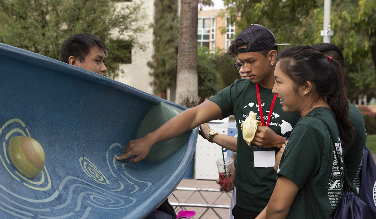 Photo of students looking at a canoe. Caption: Engineering students from the University of Hawaii’s team check out the concrete canoe featuring a theme based on the famous Vincent Van Gogh painting “Starry, Starry Night,” built by the team from California Polytechnic State University at San Luis Obispo. Photographer: Erika Gronek/ASU
