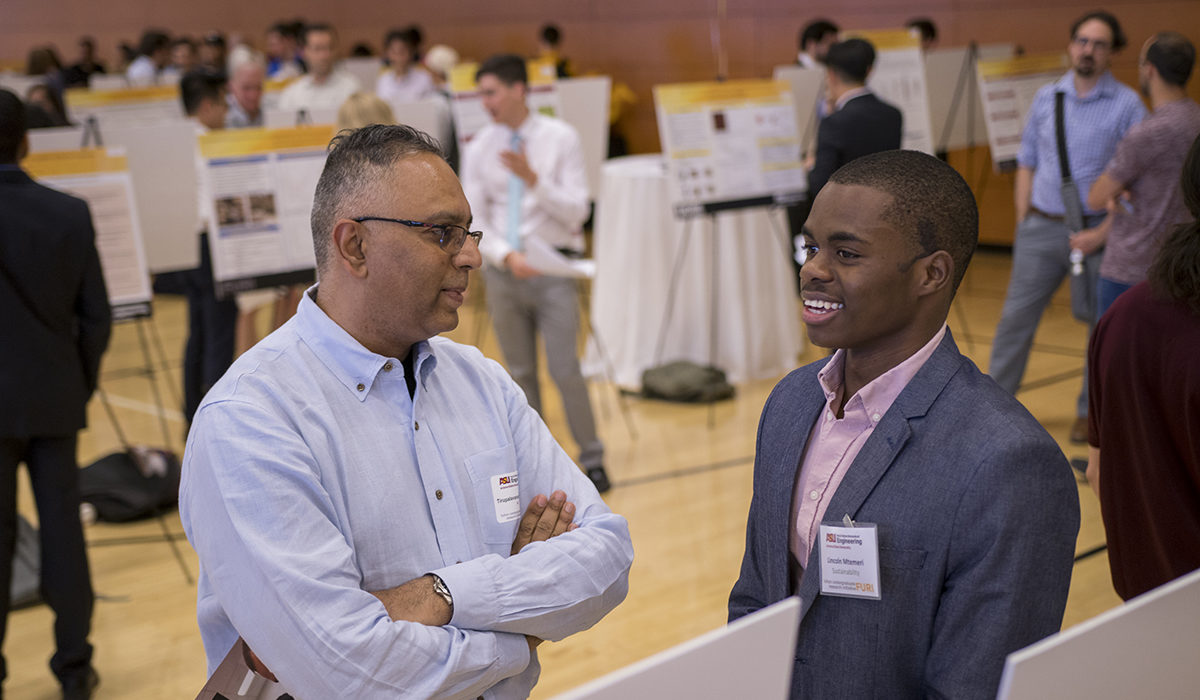 Photo of professor talking to student. Caption: Associate Research Professor and mentor Tirupalavanam Ganesh discusses research with chemical engineering student Lincoln Mtemeri at the FURI Symposium. Mtemeri, an international student from Zimbabwe, studied cost-effective catalysts for wastewater treatment technology that could deliver better clean water security and produce useful byproducts such as hydrogen for developing nations. Photographer: Marco-Alexis Chaira/ASU