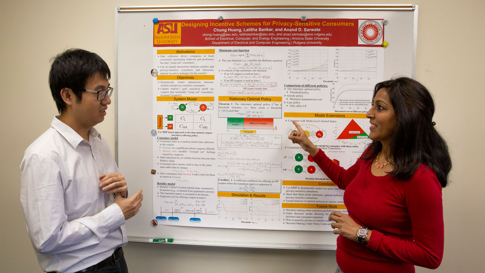 Lalitha Sankar and Chong Huang talk in front of a research poster.