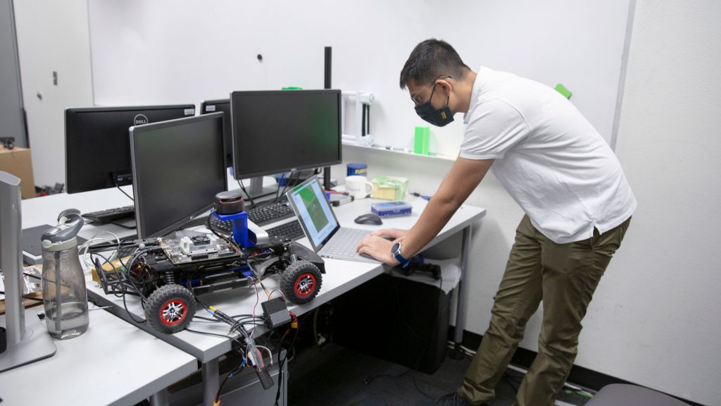 Computer science graduate student Parth Khopkar works with a laptop and a small autonomous vehicle in the lab.