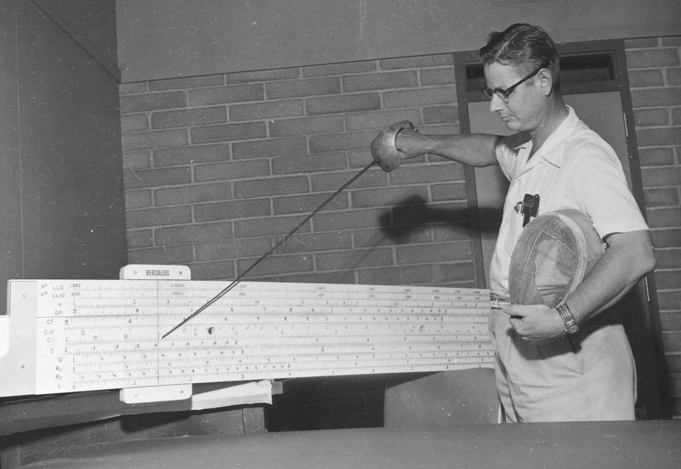 George Beakley Jr. pointing at a 10-foot-long slide rule with a sword