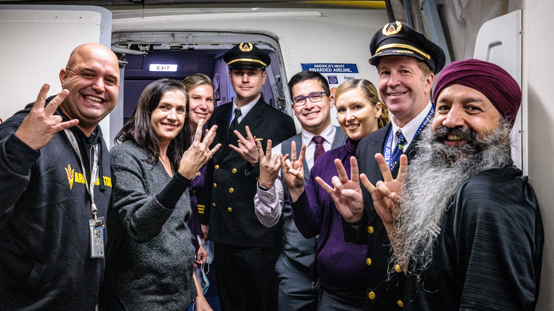 A group of people poses on an airplane while doing the ASU pitchfork hand sign.