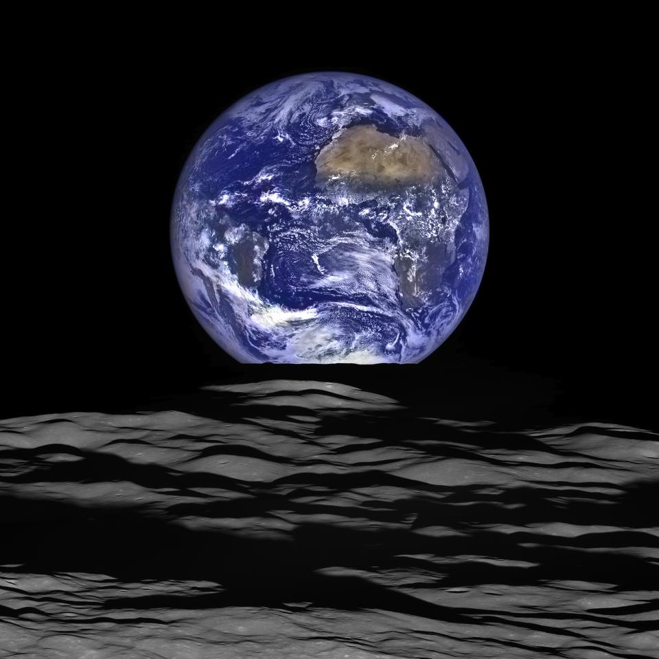 A full Earth straddles the edge of the moon, as seen from lunar orbit. On Earth, Africa and South America are visible.