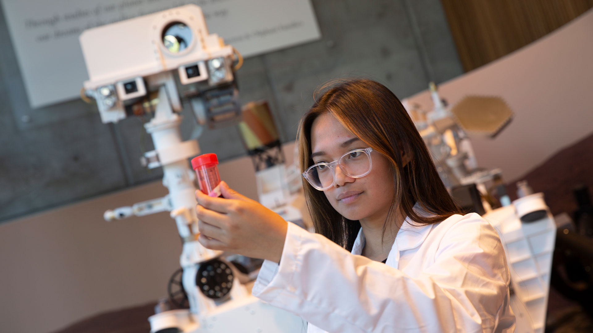 Biomedical engineering student Joy Agus stands in front of a model of a Mars rover with a vial of red liquid, demonstrating her research in the FURI program at the Ira A. Fulton Schools of Engineering at ASU.
