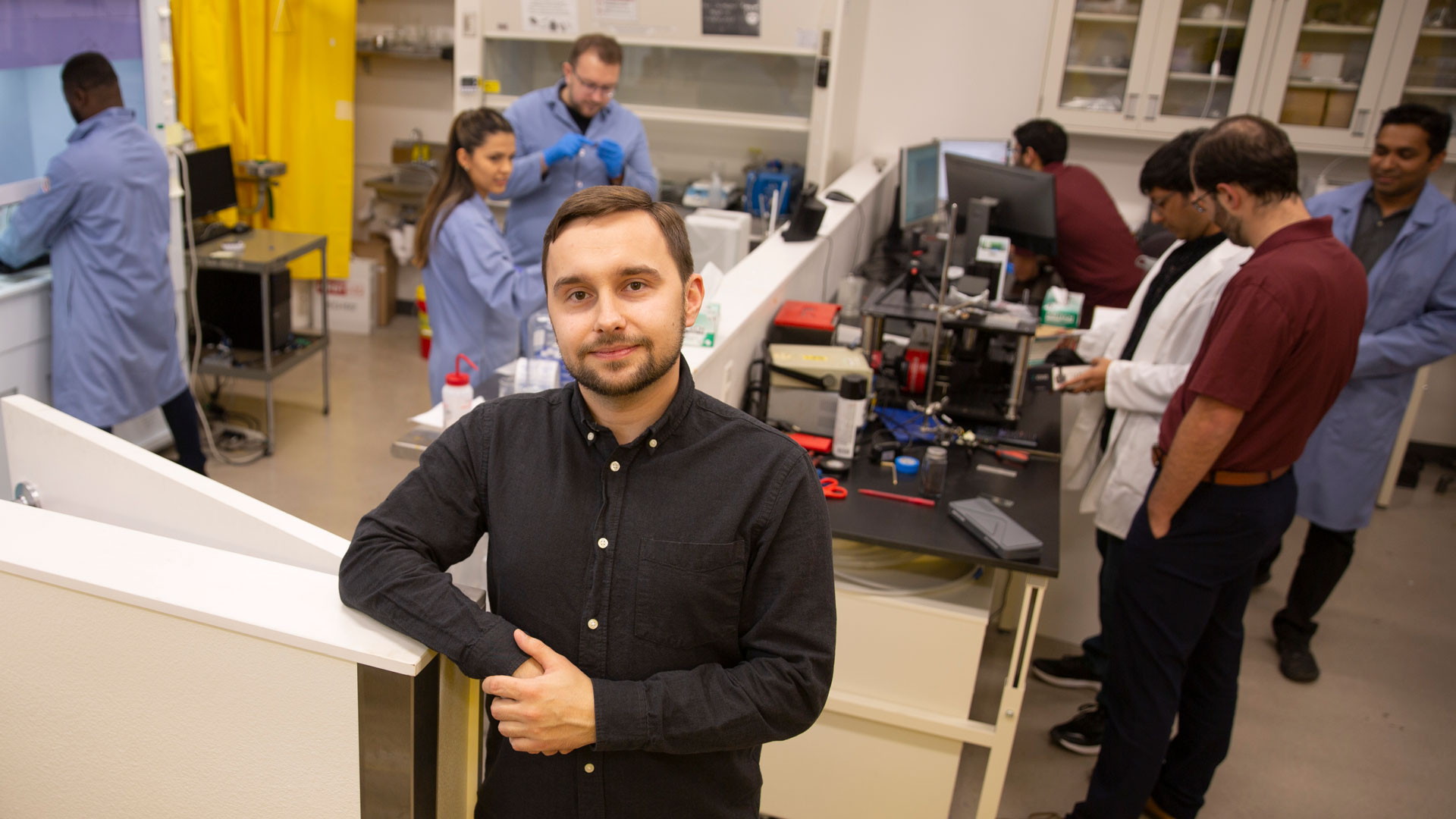 Aliaksandr "Sasha" Sharstniou poses in Assistant Professor Bruno Azeredo's lab while other students work in the background.