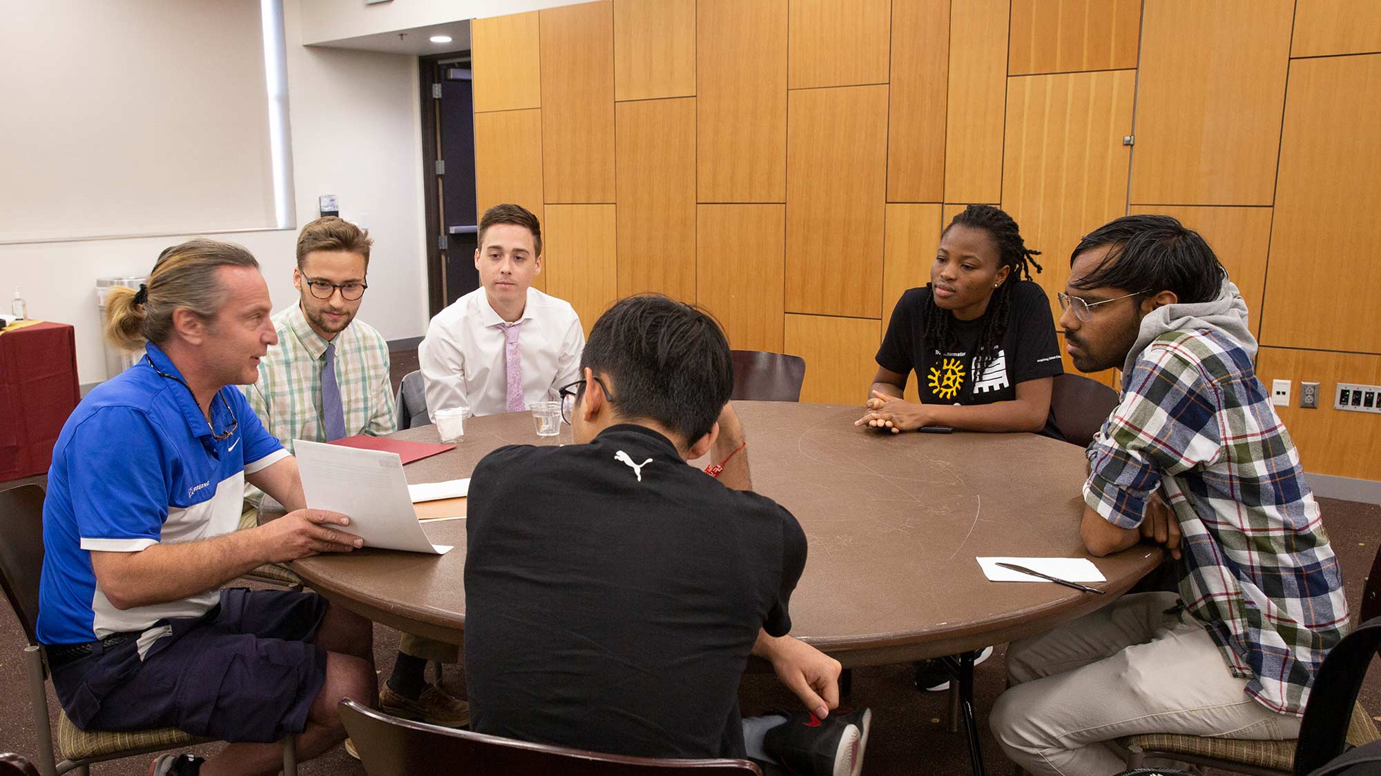 A group of students learns from an engineer about the career field while seated around a table