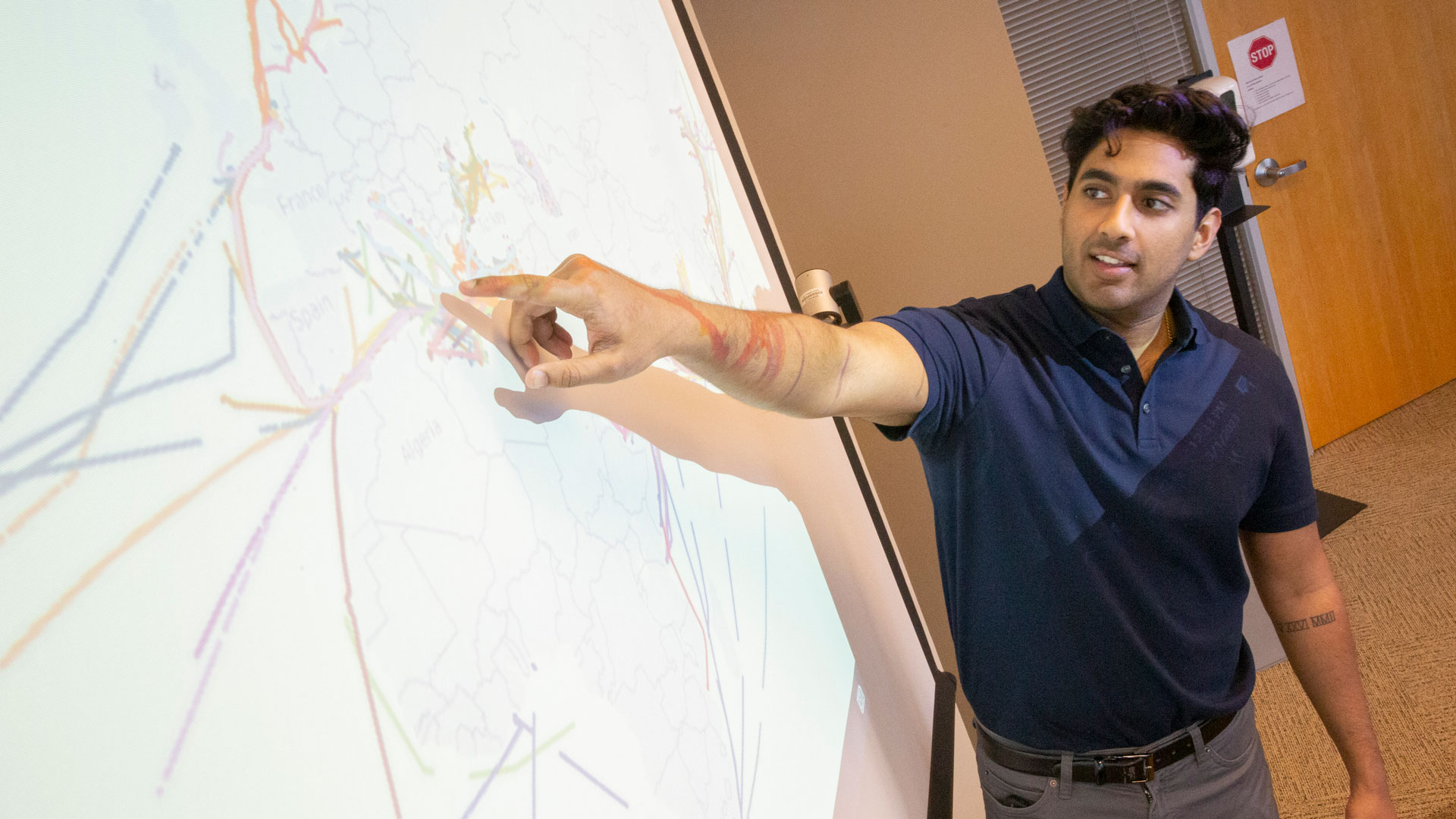 ASU computer science student Rohan Nair points at a projection screen displaying shipping routes.