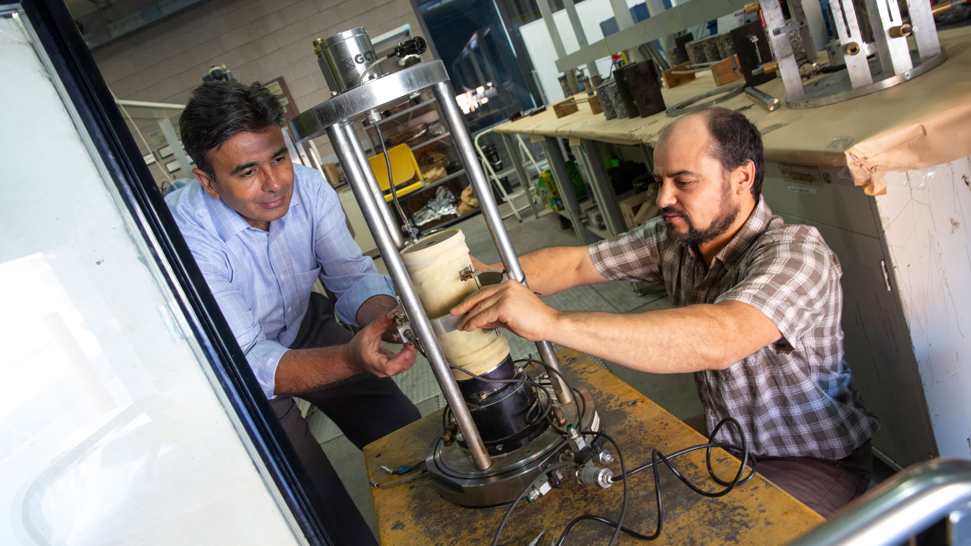 ASU faculty researcher Hasan Ozer and civil, environmental and sustainable engineering graduate student Ashraf Alrajhi prepare a pavement sample in the dynamic triaxial testing system.