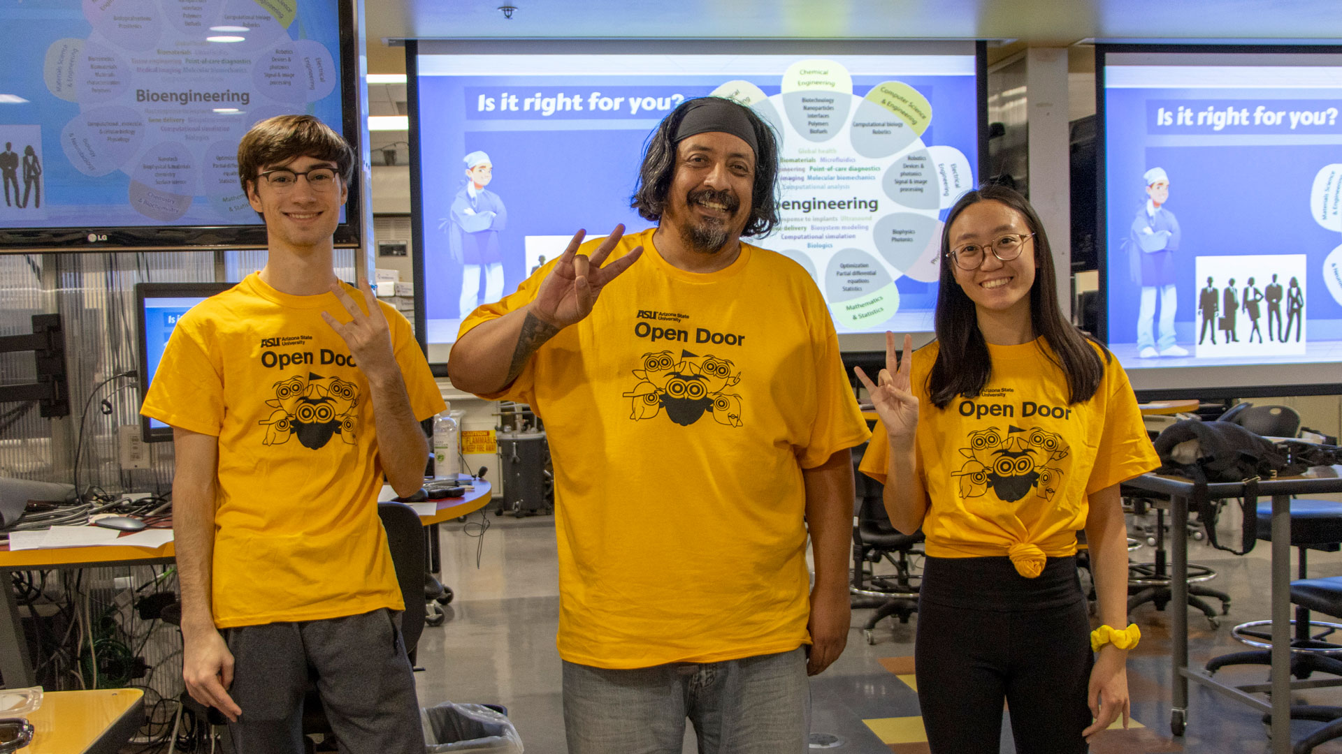 Three engineering students in gold t-shirts pose in a biomedical engineering classroom at ASU.