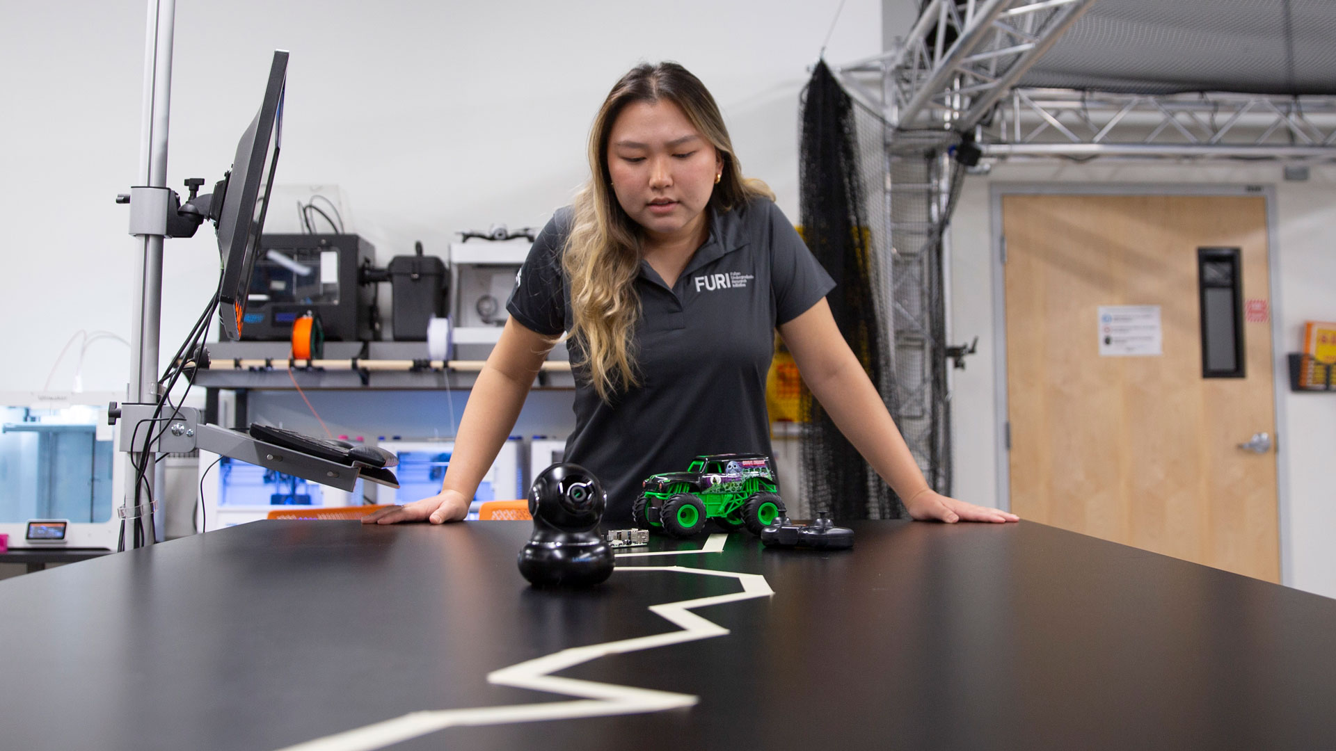 FURI student Jenna Jae Eun Lee works in a lab space with a remote control car and camera.