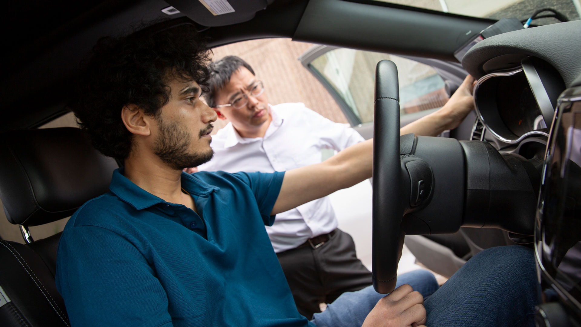 Graduate student Rohit Menon sits in an autonomous car while his mentor Yan Chen looks in.