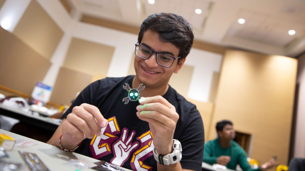 A student holds a glowing electronic part at a microelectronics workshop.